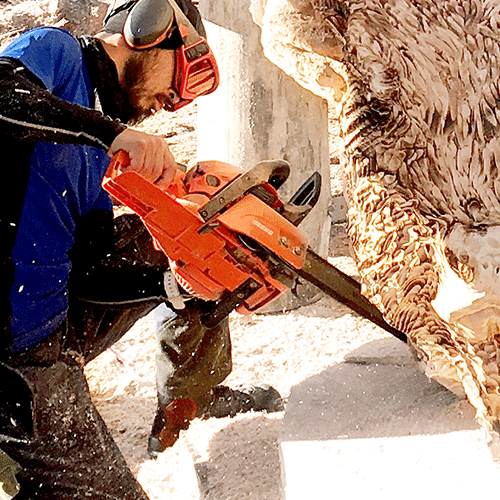 Man carving a pig using a chainsaw with a Sculptor Guide Bar
